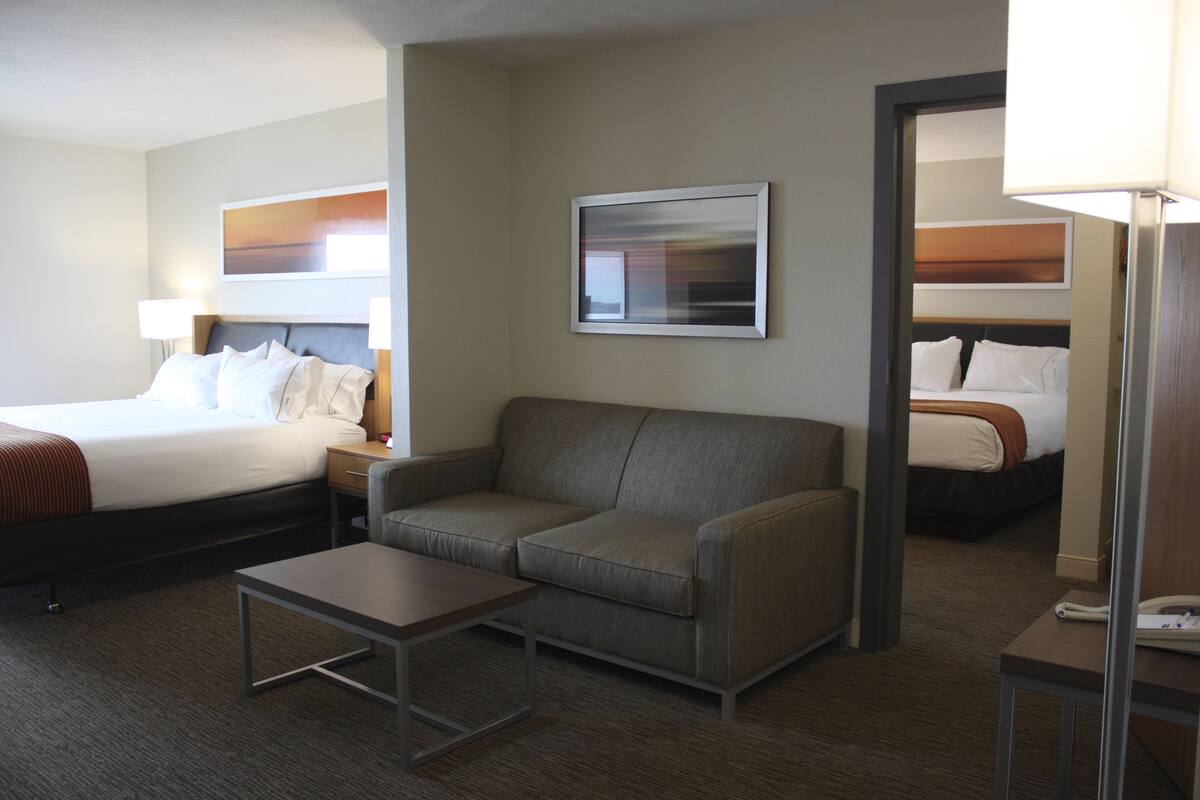A hotel room with a bed, a sofa, a small table, and a mirror.