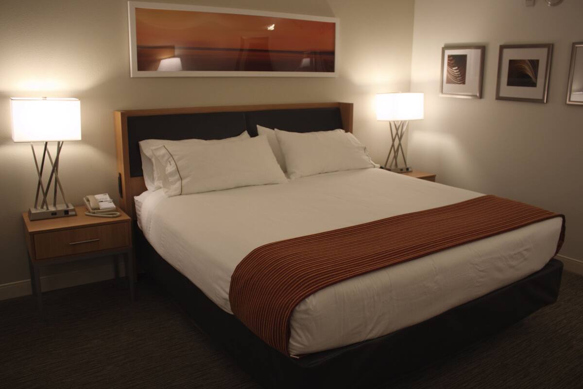 A hotel room with a large bed, two bedside tables with lamps, a telephone, and framed artwork on the wall.