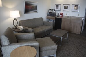 A compact hotel room with a sofa, a small table, a microwave, a coffee maker, and a sink. - Holiday Inn Express Munising-Lakeview by IHG (Munising)