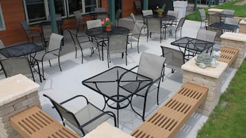 Ein Terrassenbereich im Freien mit mehreren Tischen und Stühlen, einige davon mit Kissen.