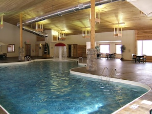 An indoor swimming pool with a stone pillar, a water feature, and a dining area with tables and chairs. - Holiday Inn Express Munising-Lakeview by IHG (Munising)