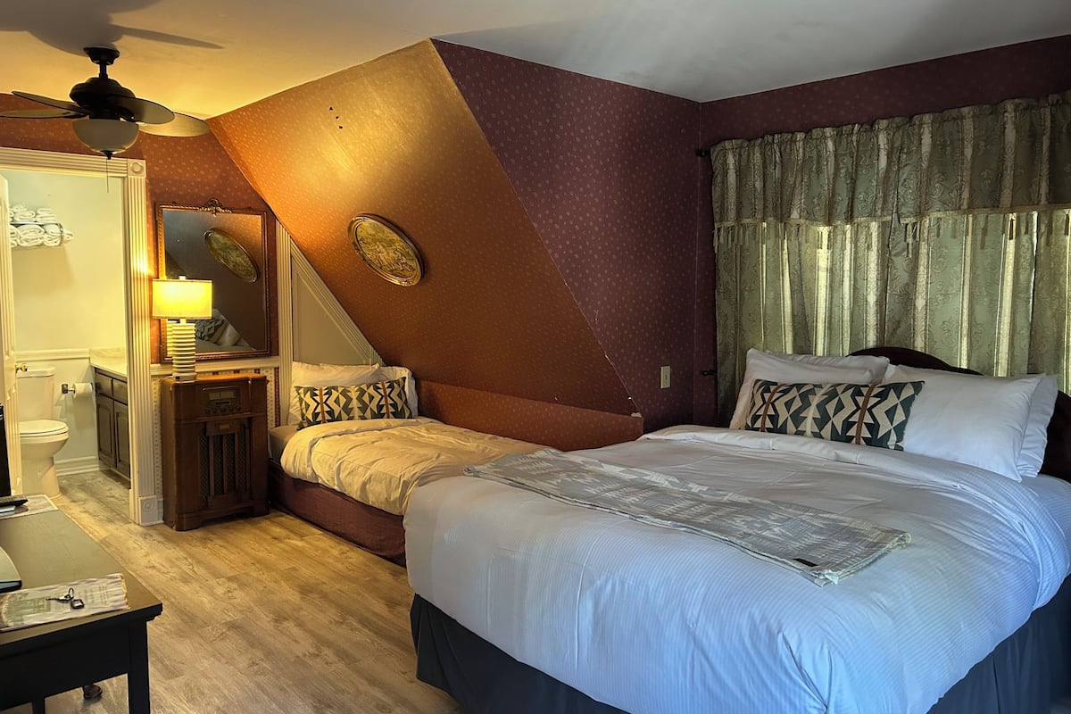 A bedroom with a large bed, a nightstand, a mirror, a ceiling fan, and a window with curtains.