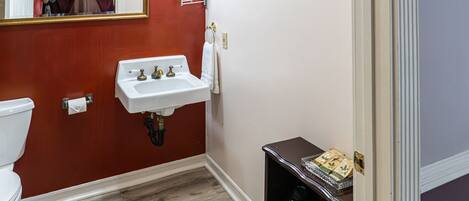 A bathroom with a white sink, a mirror, a toilet, and a wooden floor.