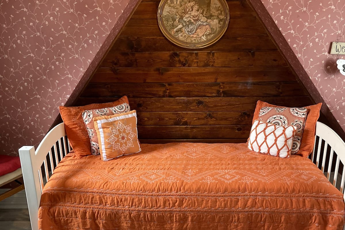 A loft-style bedroom with a sloped ceiling, a wooden headboard, and a patterned orange bedspread.