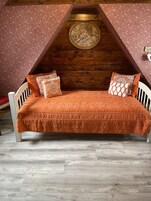 Camera da letto in stile loft con soffitto spiovente, una testiera in legno e una coperta a letto arancione con motivo.