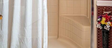 Un área de ducha con puerta de vidrio, baldosas color crema y cabezal de ducha.