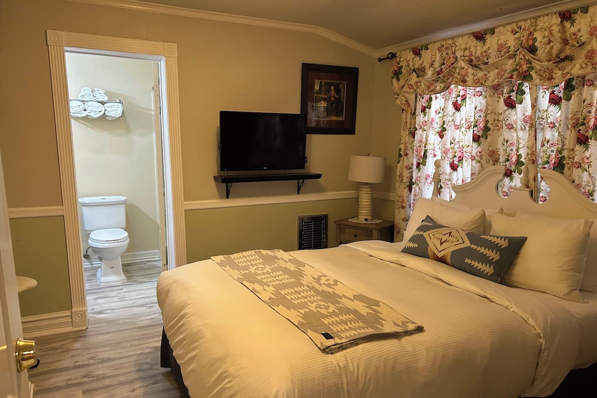 A bedroom with a bed, a television, a nightstand, a lamp, and a door leading to a bathroom.