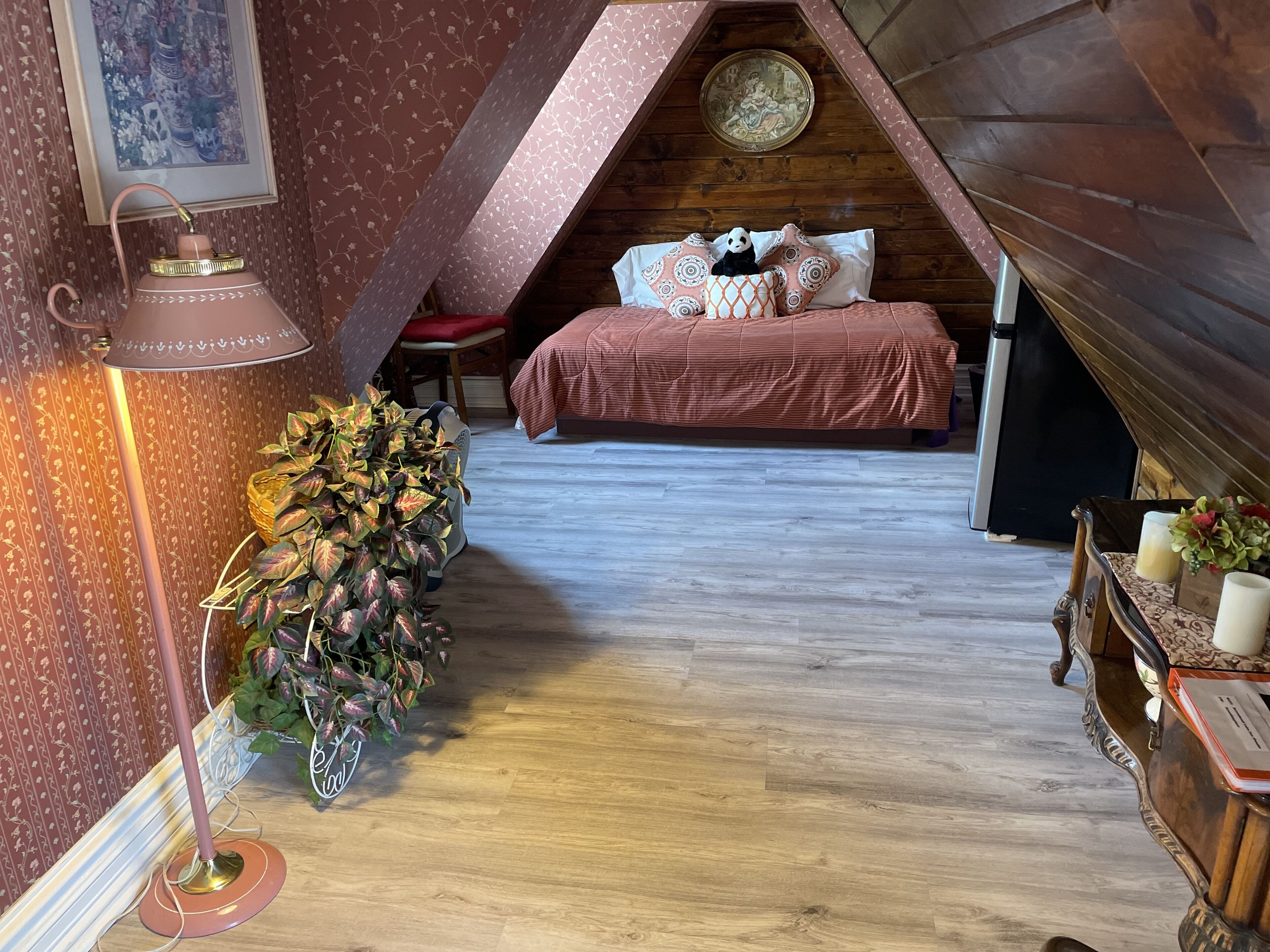 A cozy attic bedroom with a sloped ceiling, a bed with patterned bedding, a floor lamp, and a decorative plant.