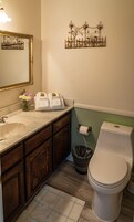 A bathroom with a marble sink, dark wooden cabinets, a white toilet, and a wall-mounted light fixture.