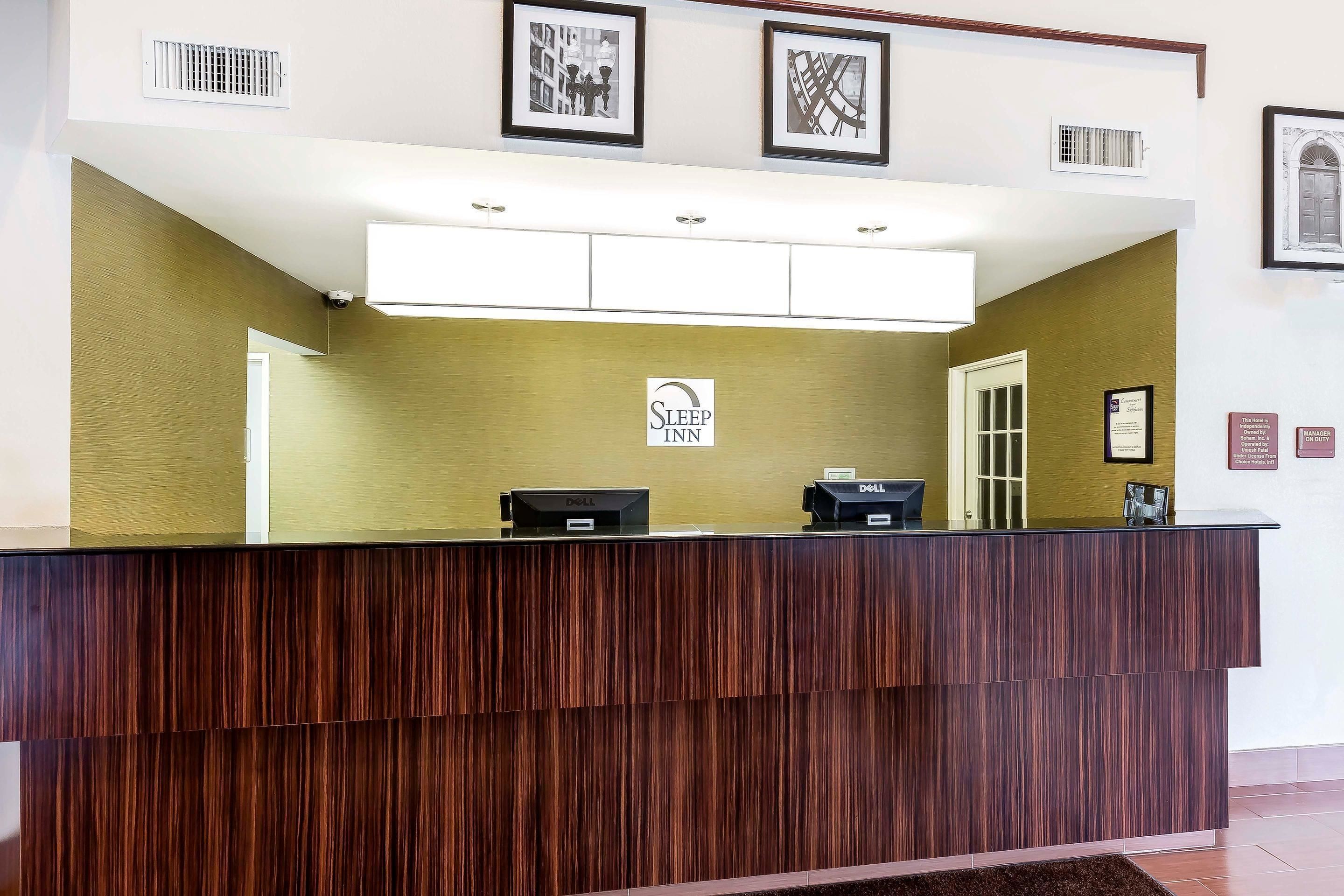 A reception desk with a wooden finish, a sign for Sleep Inn, and two Dell computers.