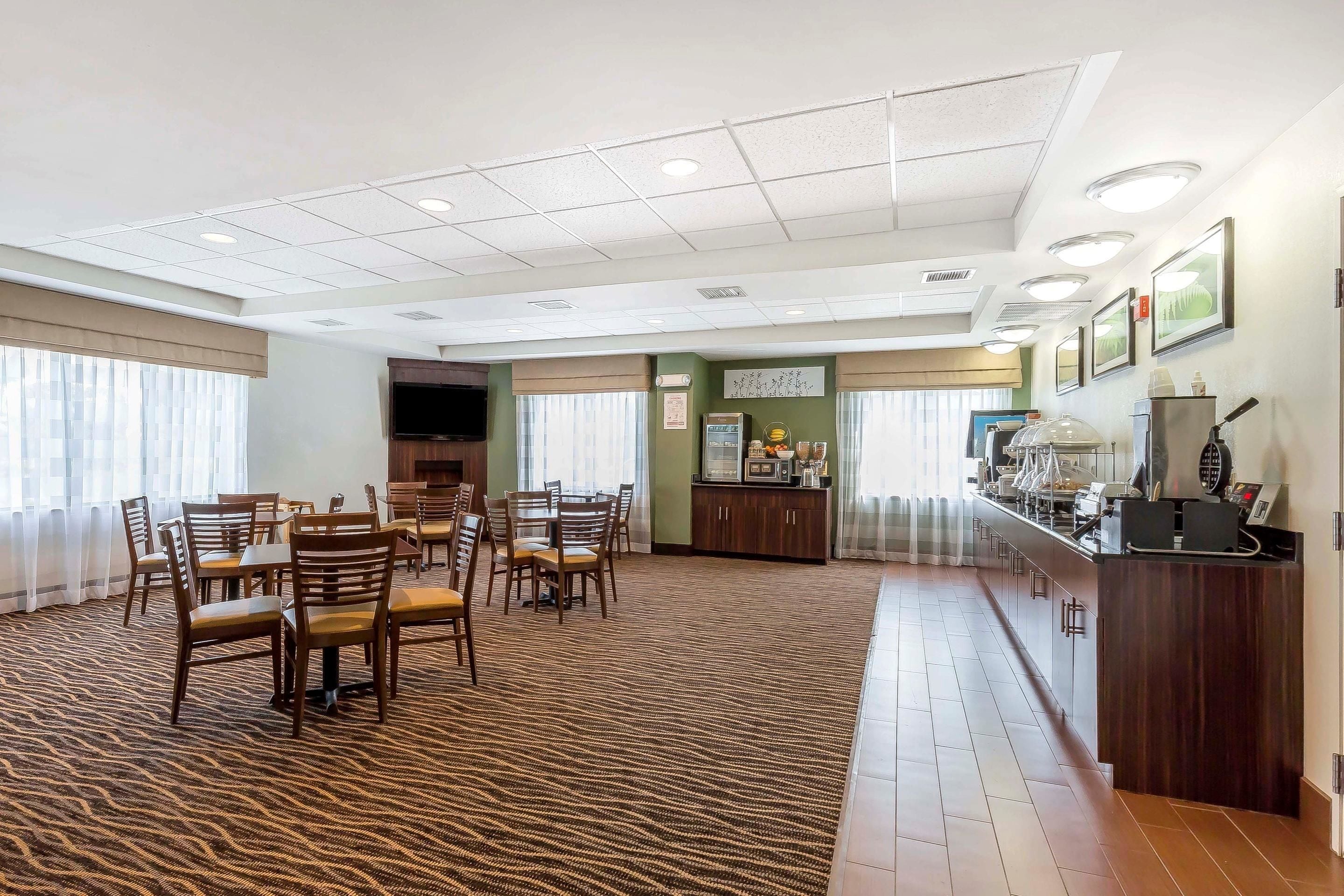 A hotel dining area with multiple tables and chairs, a reception desk, and a kitchen area.