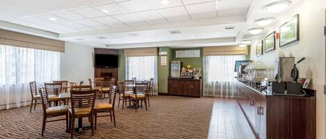 A hotel dining area with multiple tables and chairs, a reception desk, and a kitchen area.
