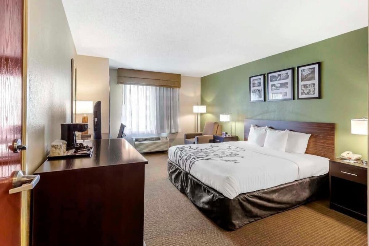 A hotel room with a bed, desk, bedside tables, lamps, and framed pictures on the wall.