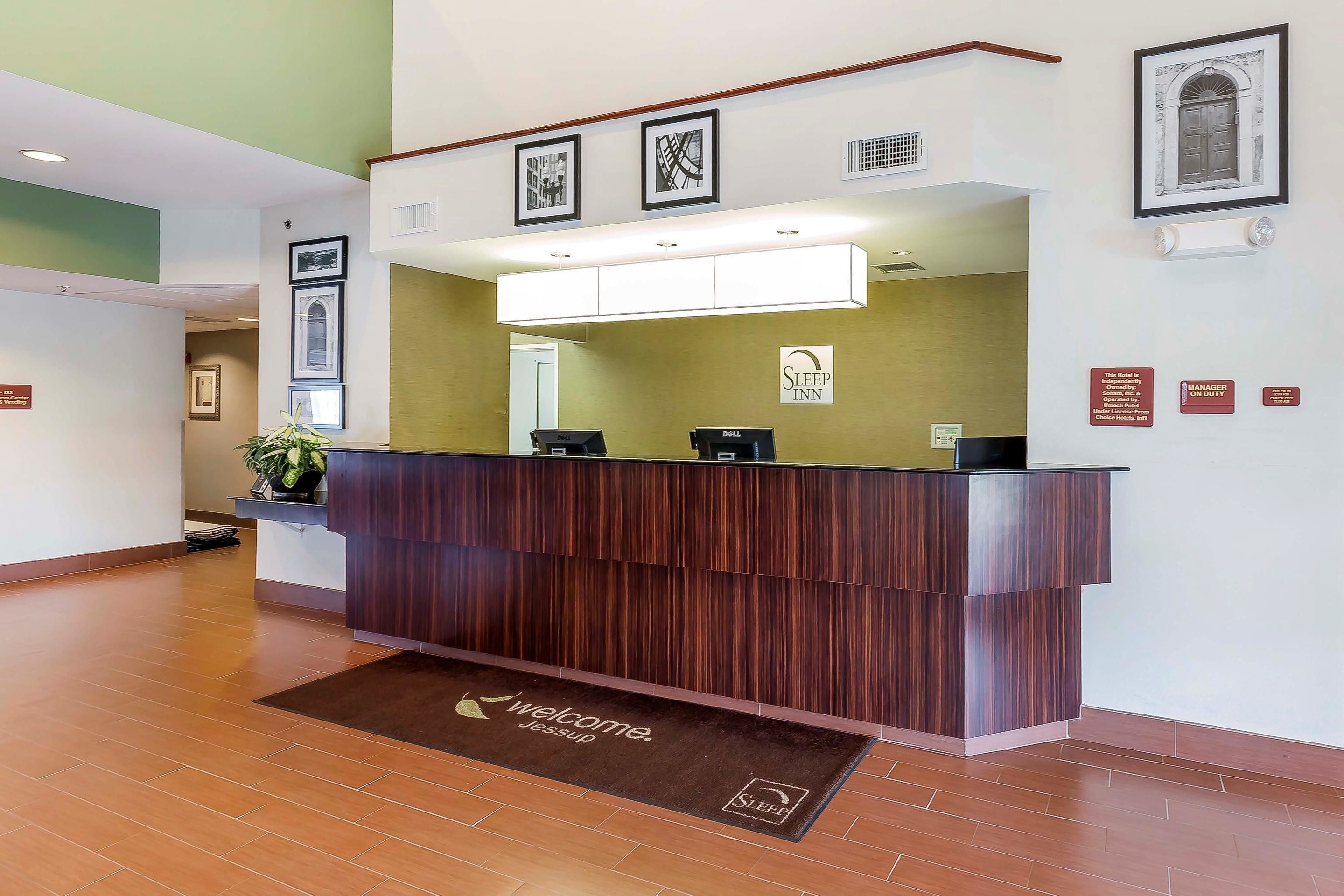 A reception desk with a wooden finish, a welcome mat, and framed pictures on the wall.