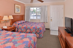 A hotel room with two beds, a television, a desk with a lamp, and a window with curtains.