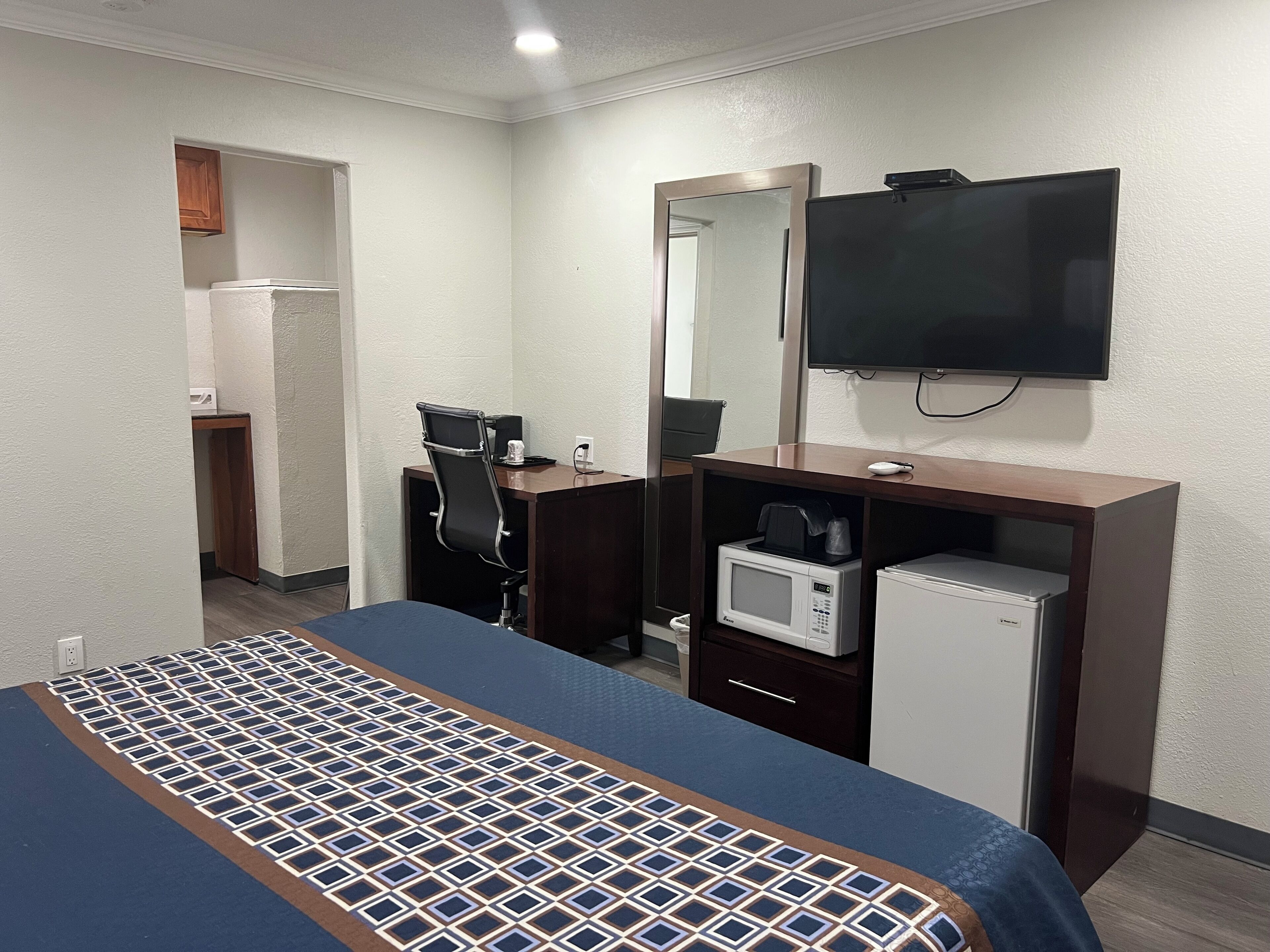 Ein Hotelzimmer mit Bett, Schreibtisch mit Stuhl, Mikrowelle, Fernseher und kleinem Kühlschrank.