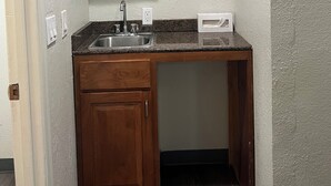 A compact kitchen with wooden cabinets, a granite countertop, a stainless steel sink, and a built-in microwave.