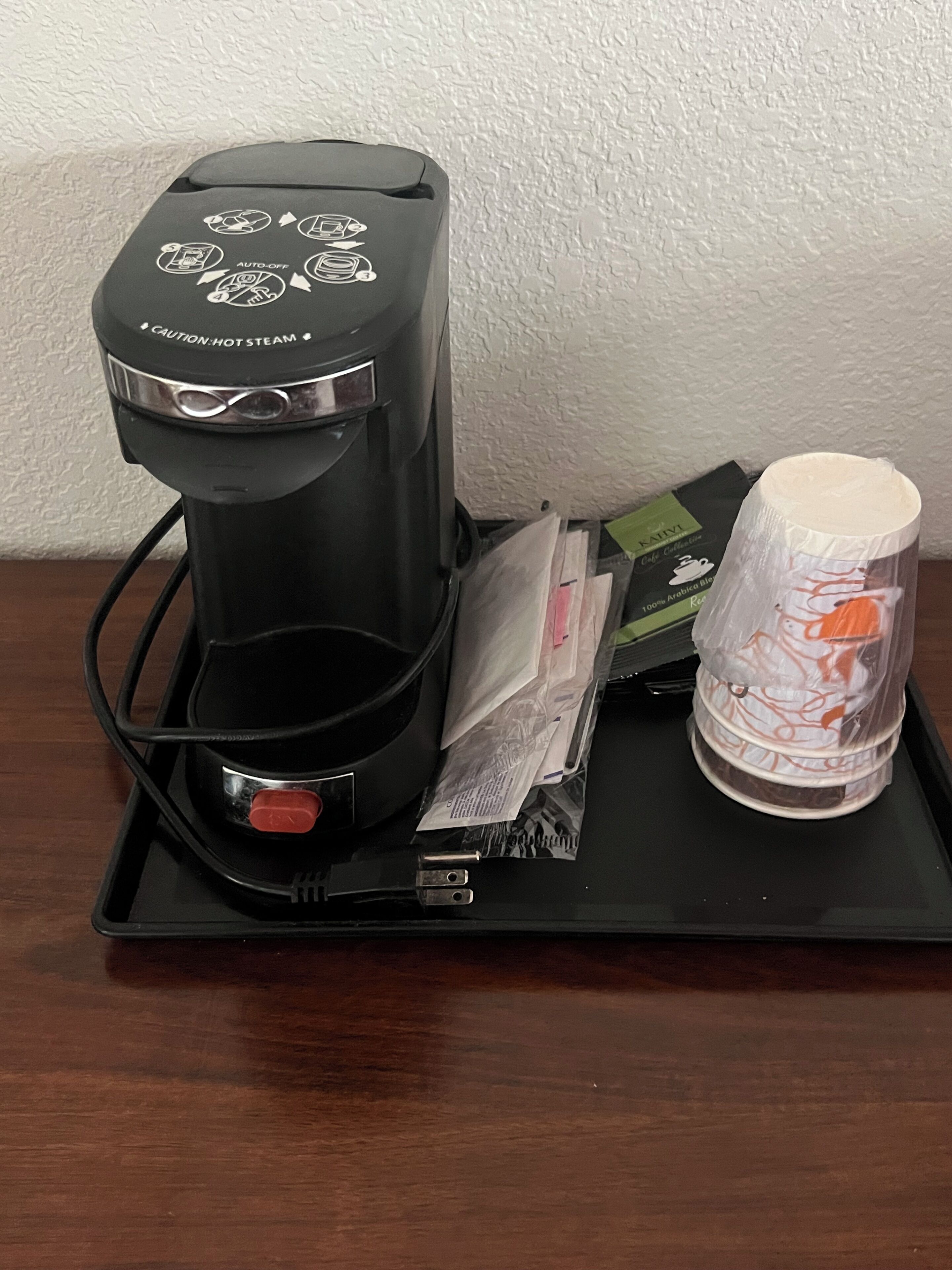 Una macchina per il caffè con un vassoio, una capsula di caffè e una tazza di plastica su un tavolo.