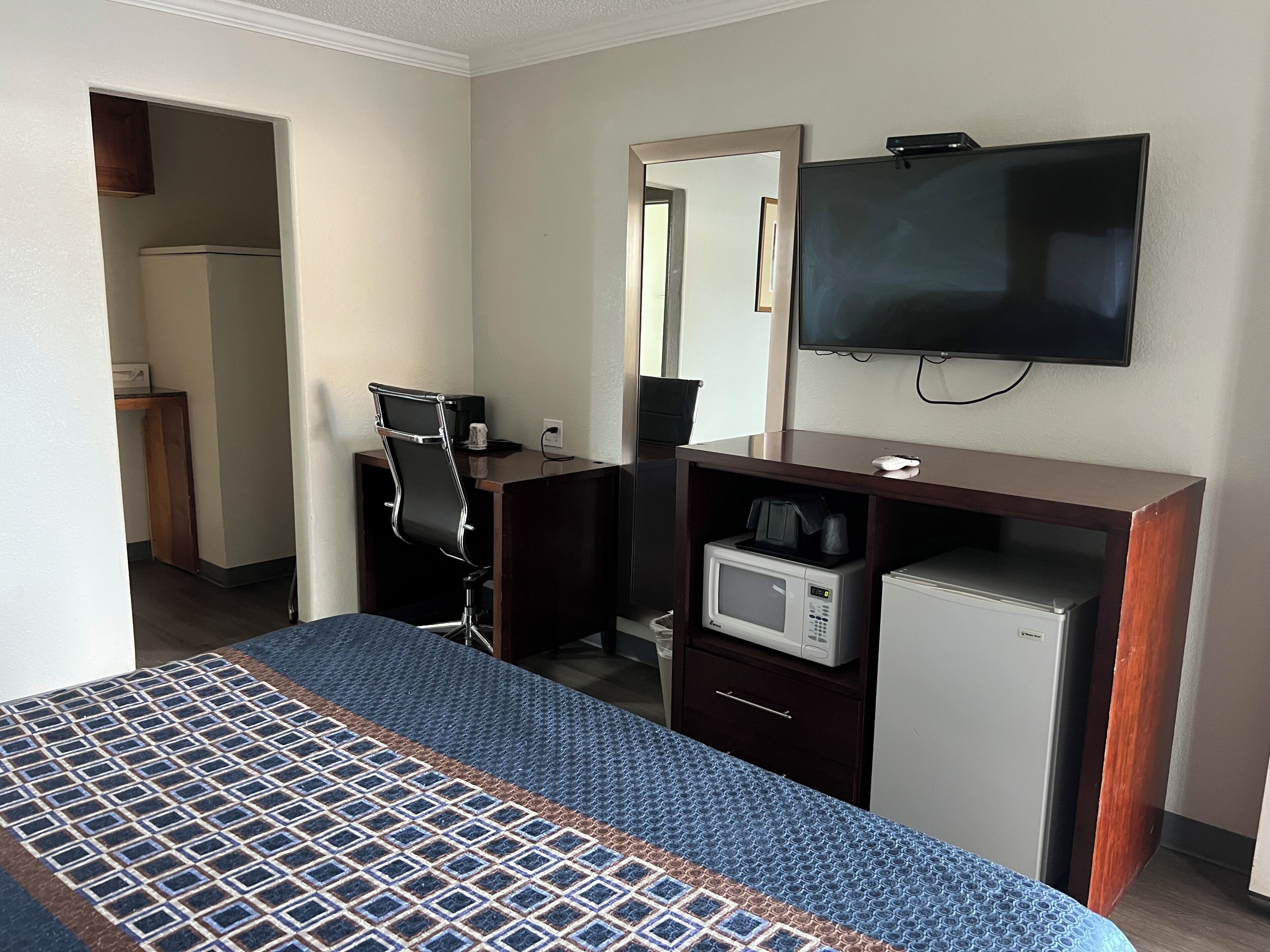 Habitación de hotel con cama, escritorio con computadora, microondas, televisión y refrigerador pequeño.