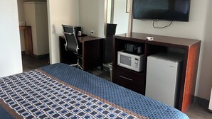 Ein Hotelzimmer mit einem Bett, einem Schreibtisch mit Computer, einer Mikrowelle, einem Fernseher und einem kleinen Kühlschrank.