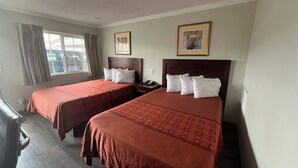 A hotel room with two beds, a window with curtains, and two framed pictures on the wall.