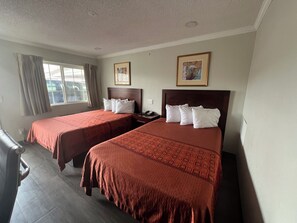 Una habitación de hotel con dos camas, una ventana con cortinas y dos cuadros en la pared.