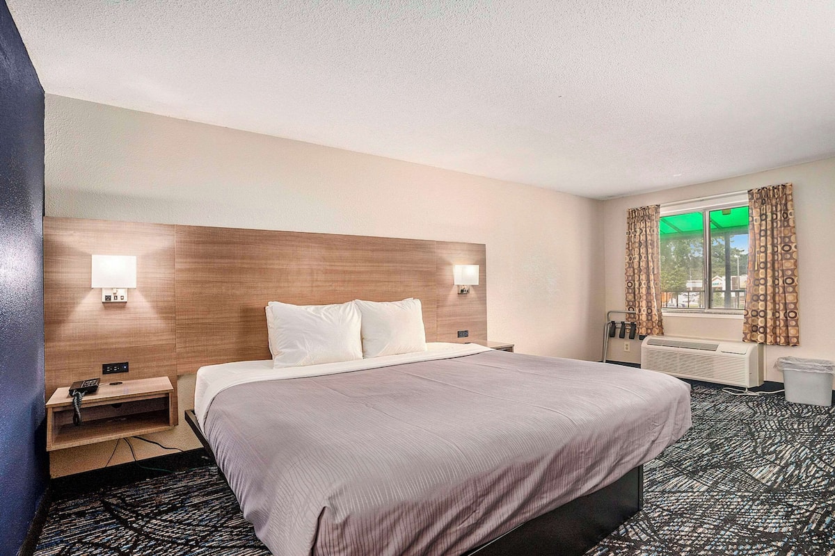 Quarto de hotel com uma cama grande, mesas de cabeceira, uma janela com cortinas, um radiador e um telefone fixado na parede.