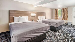 A hotel room with two beds, a headboard, a nightstand, a lamp, and a window with curtains. - Rodeway Inn Grand Haven (Grand Haven)