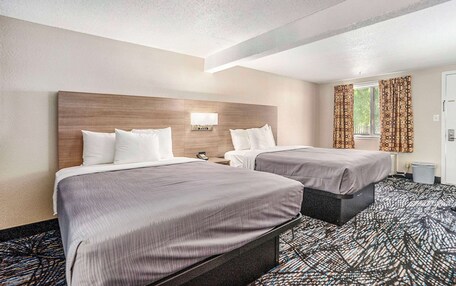 A hotel room with two beds, a headboard, a nightstand, a lamp, and a window with curtains.