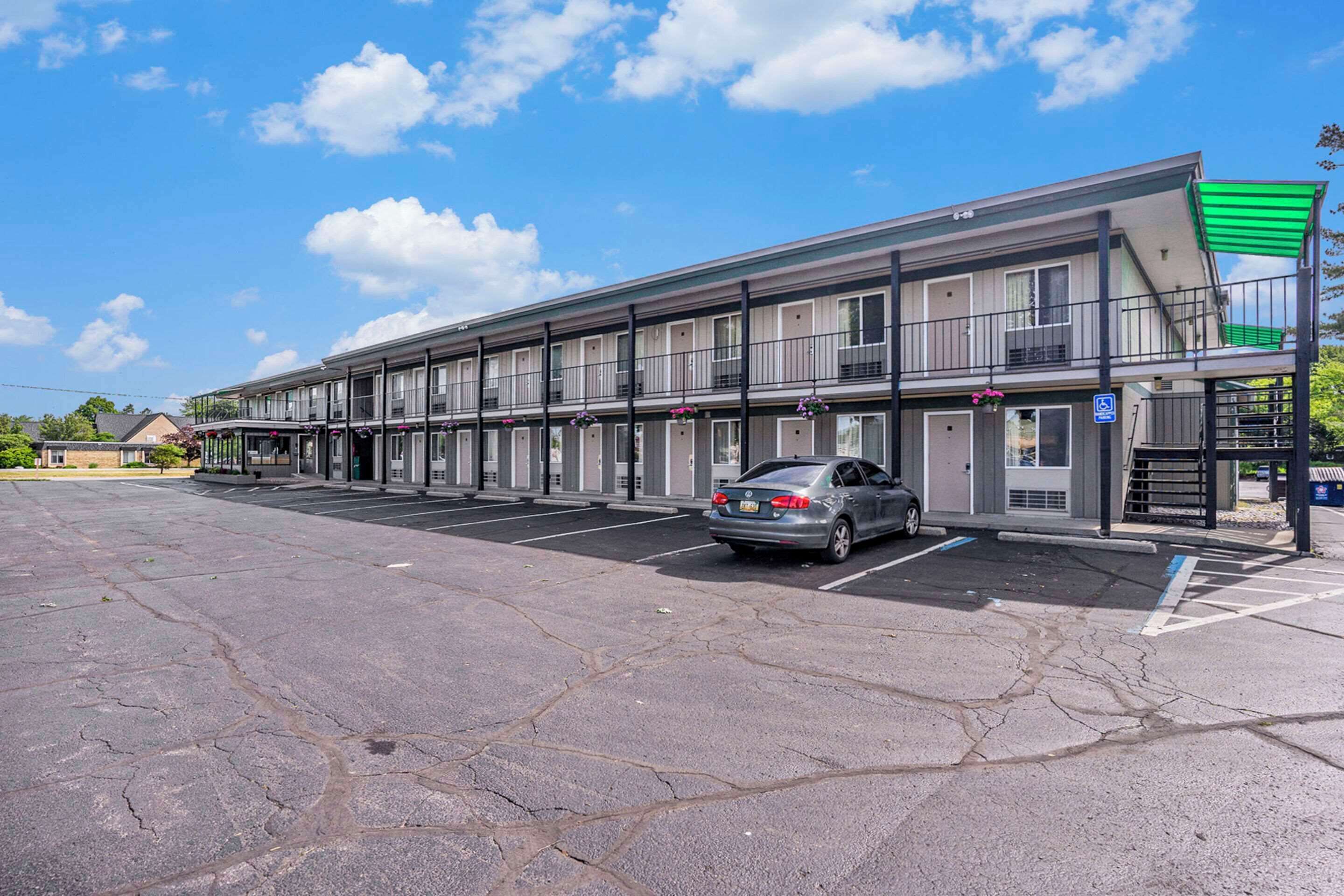 A multi-story motel with a parking lot and a car parked in front.