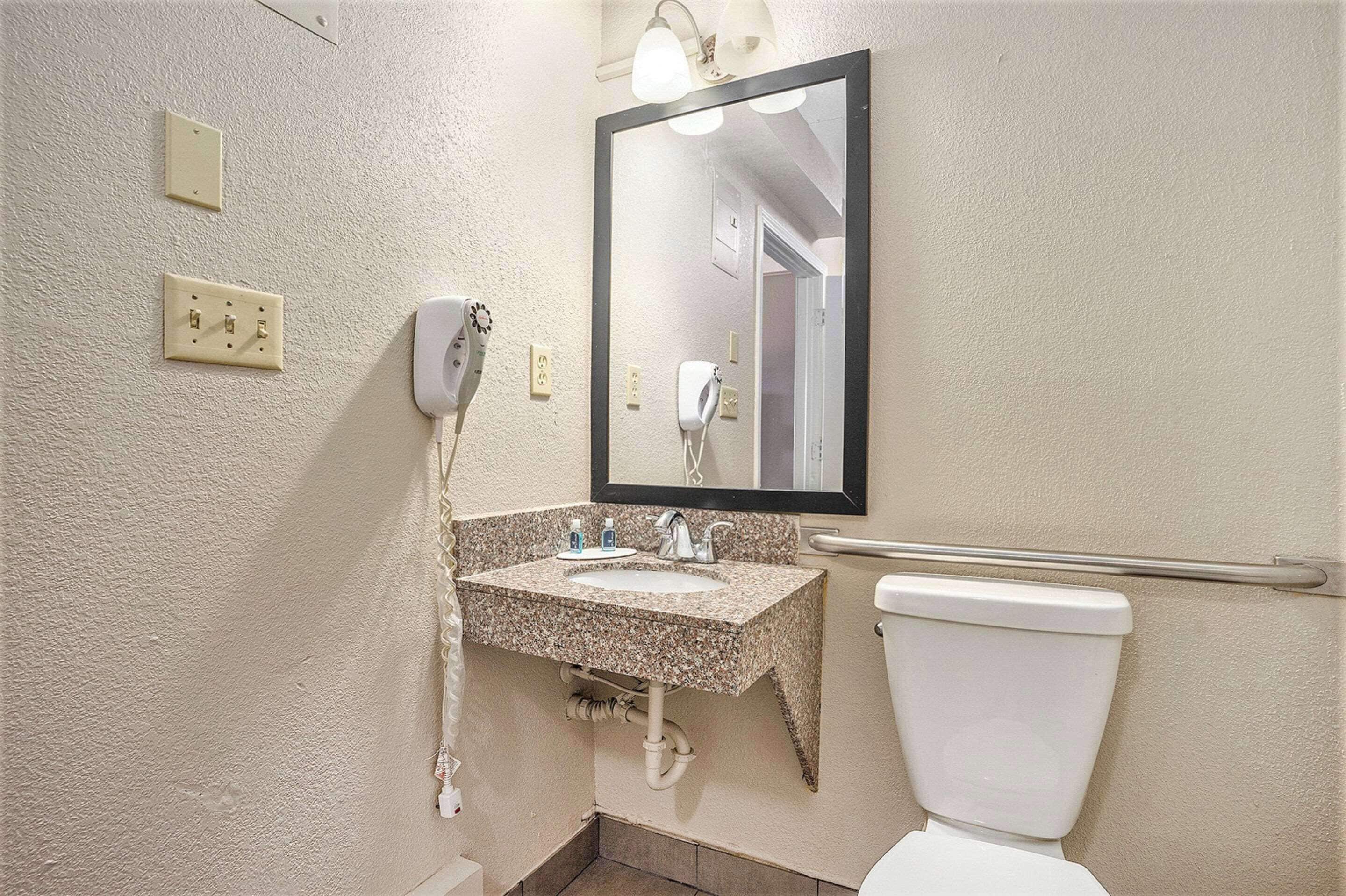 A bathroom with a sink, mirror, hairdryer, and toilet.