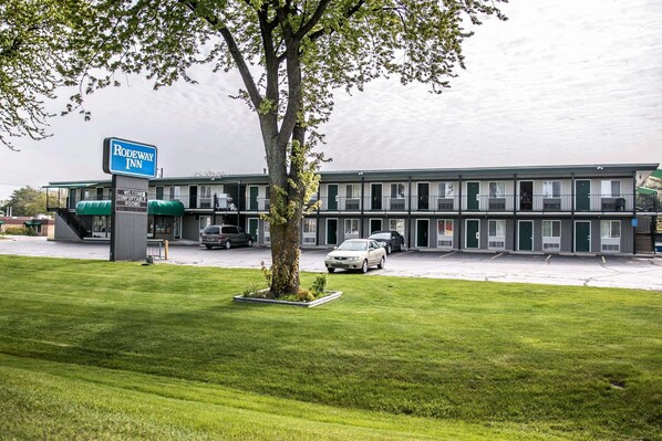 A motel with a signboard, a parking lot, and a building with multiple rooms.