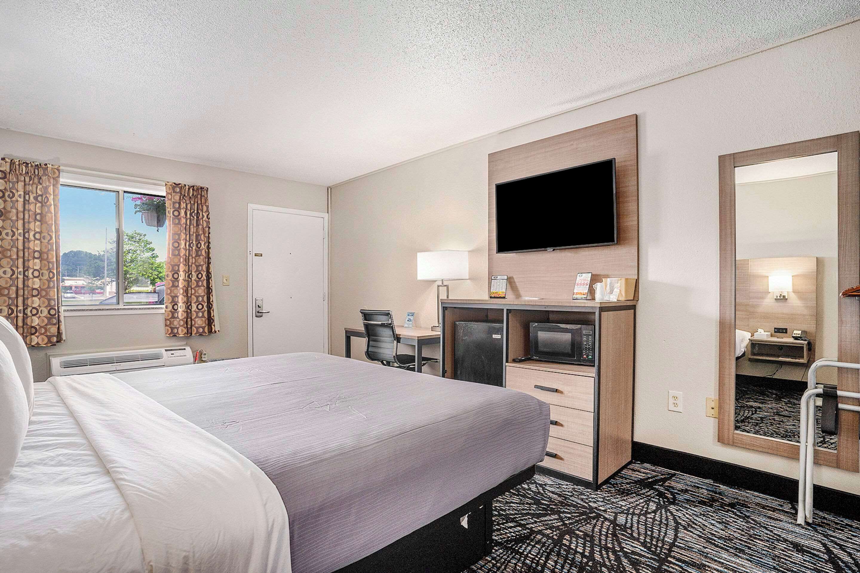A hotel room with a bed, desk, TV, and a large mirror.