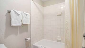 Et badeværelse med badekar, toilet og et håndklædetørrestativ med to håndklæder.