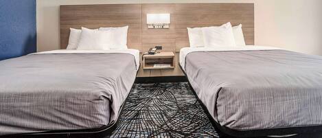 Una habitación de hotel con dos camas individuales, una mesita de noche con lámpara y una alfombra estampada.