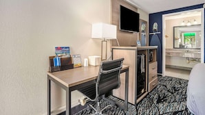 Habitación de hotel con escritorio, silla, televisión y baño con espejo y lavabo.