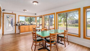Un comedor con una mesa verde y sillas de madera, ventanas amplias y vistas al exterior.
