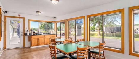 A dining area with a green table and wooden chairs, large windows, and a view of the outside.