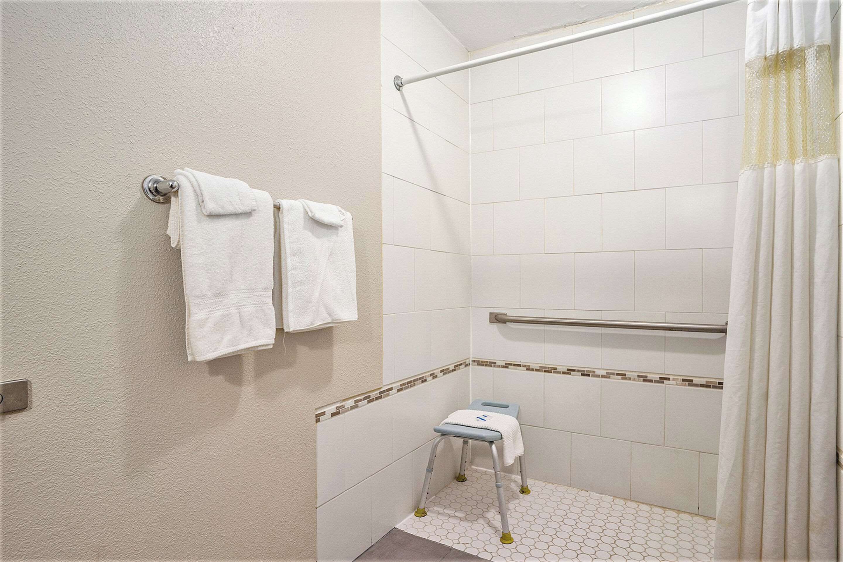 A small, white bathroom with a shower area, a grab bar, and a step stool.