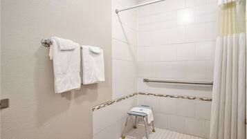 A small, white bathroom with a shower area, a grab bar, and a step stool.