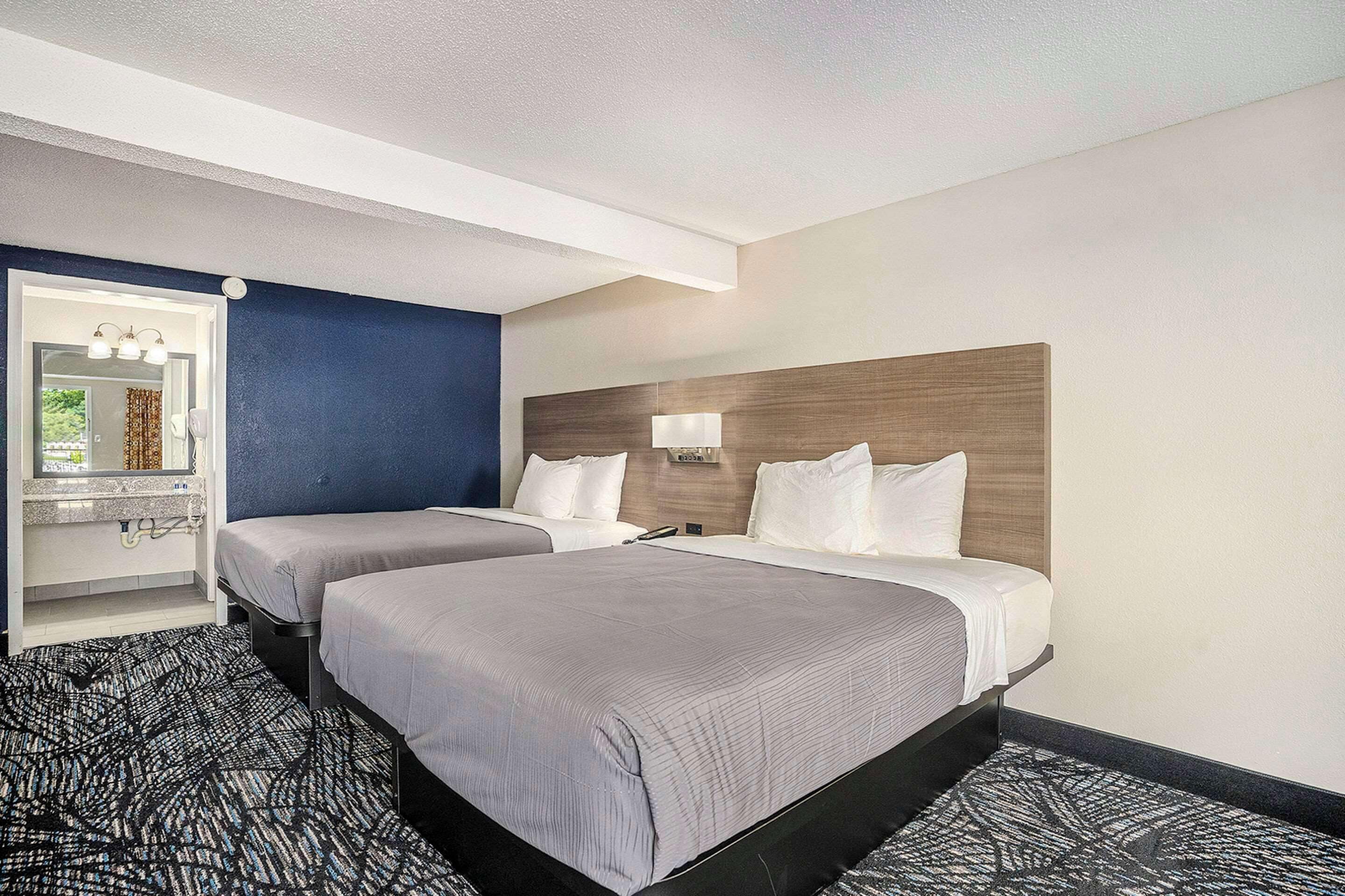 A hotel room with two beds, a bathroom with a mirror, and a patterned carpet.