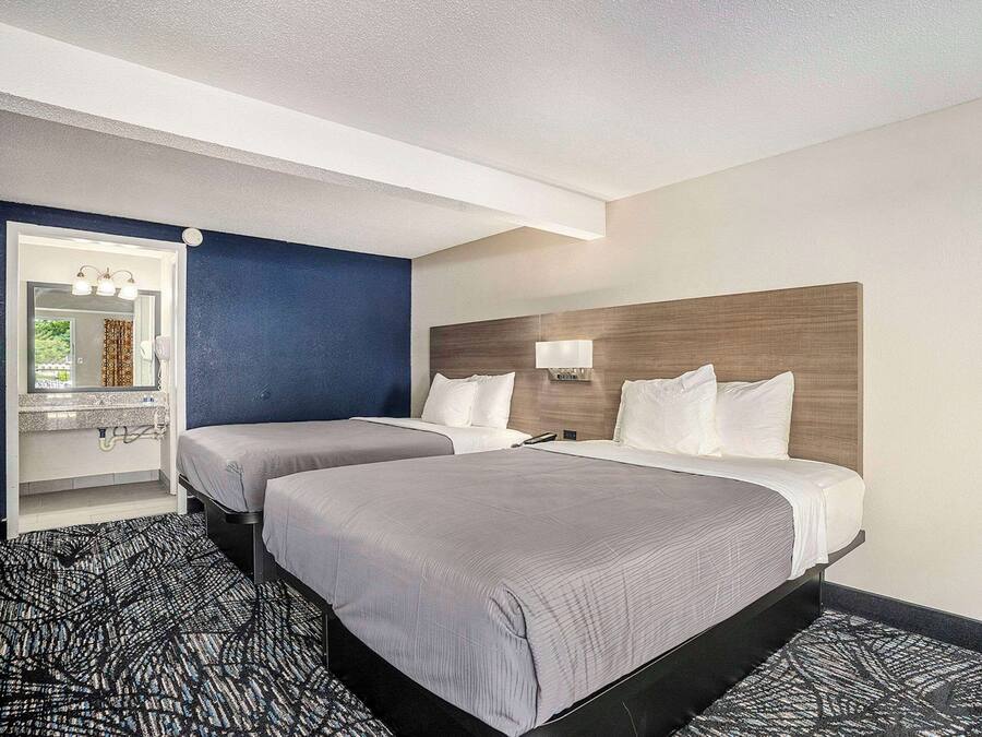 A hotel room with two beds, a bathroom with a mirror, and a patterned carpet.