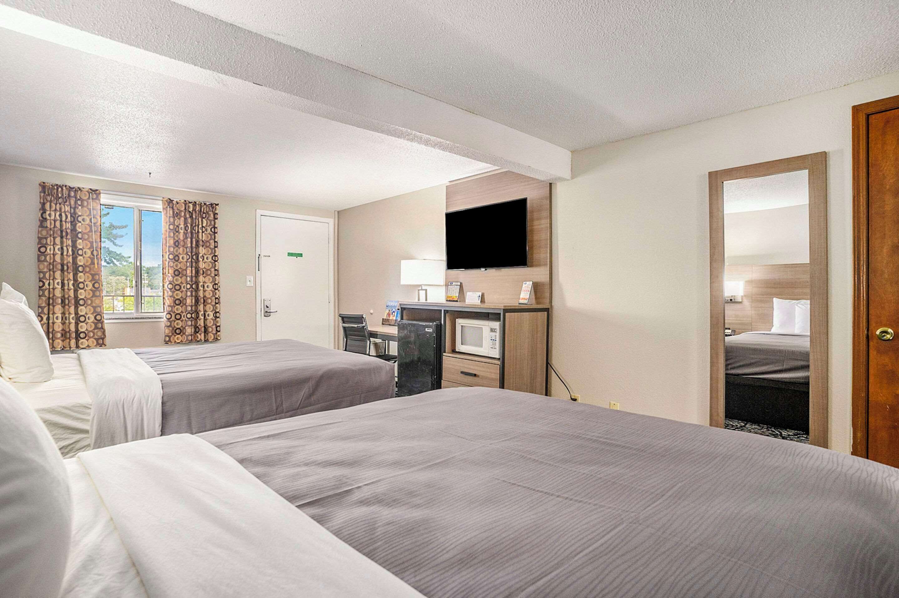 Una habitación de hotel con dos camas, un escritorio con computadora, televisor y microondas.