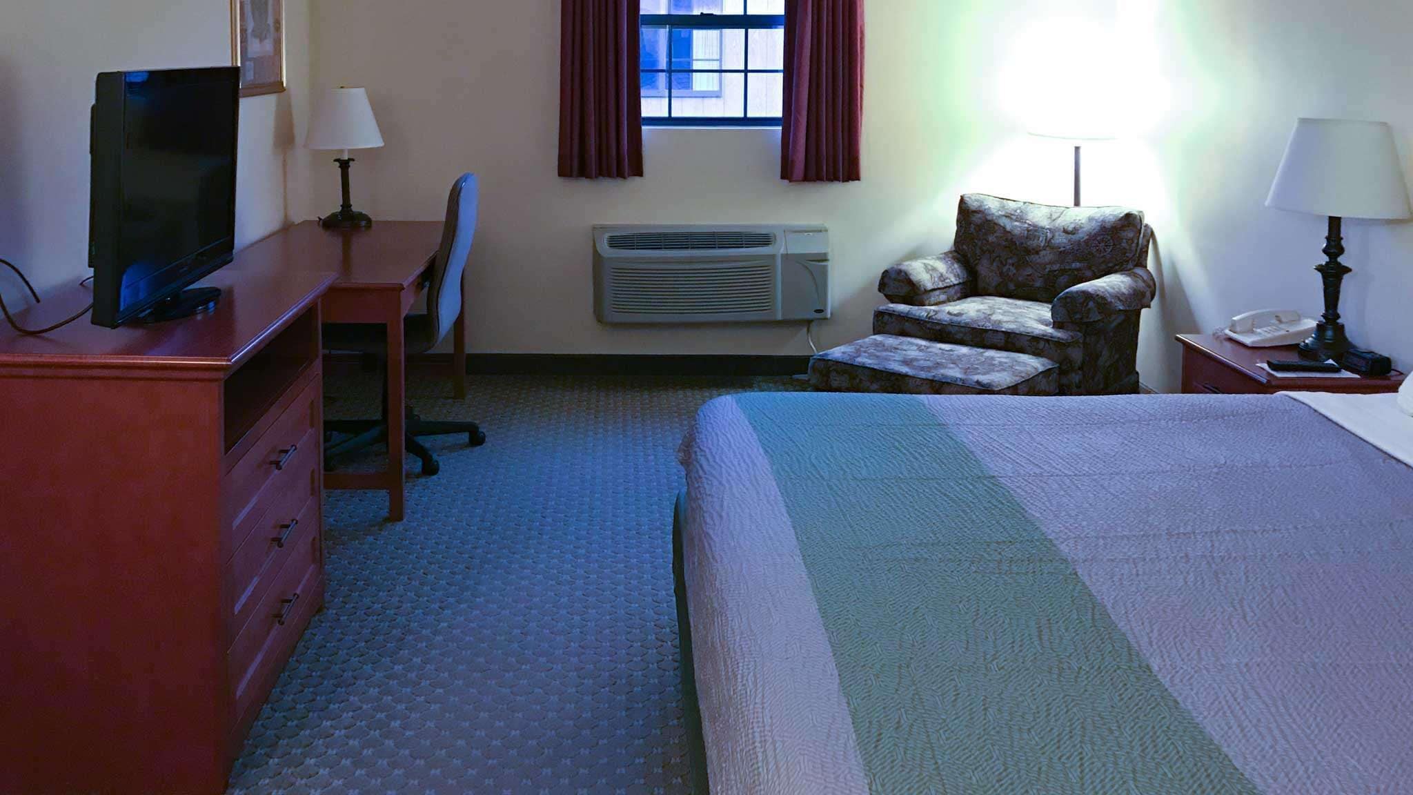 Une chambre d’hôtel équipée d’un lit, d’un bureau, d’une chaise, d’une télévision, d’un climatiseur et d’une fenêtre avec des rideaux.