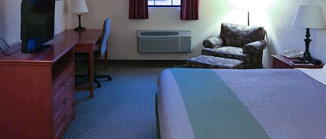 A hotel room with a bed, a desk, a chair, a television, an air conditioner, and a window with curtains.