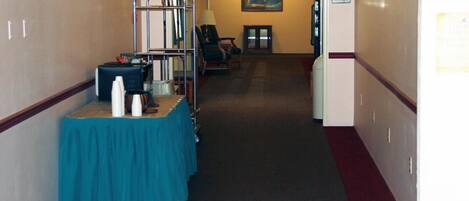 A hotel corridor with an exit sign, a reception desk, and a seating area.