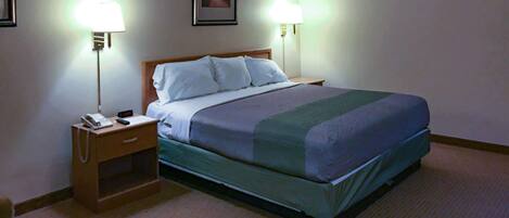 A hotel room with a bed, bedside lamps, a nightstand with a phone, and a framed picture on the wall.