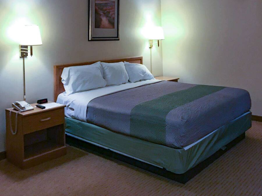 Hotelkamer met een bed, bedlampen, een nachtkastje met een telefoon en een ingelijst schilderij aan de muur.