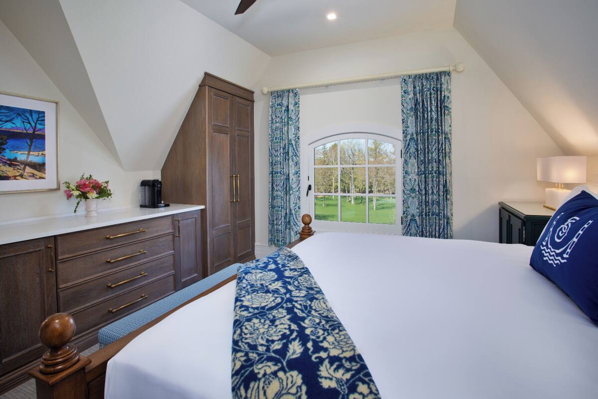 Une chambre avec un grand lit, une commode, une fenêtre avec des rideaux et un tableau au mur.