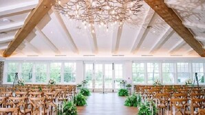 An indoor venue with wooden chairs arranged in rows, a central aisle, and a ceiling with exposed beams and a chandelier. - The Inn At Stonecliffe (Mackinac Island)